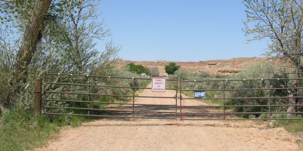 Primer plano de la puerta de entrada metálica del Rancho Skinwalker con un cartel de "No Trespassing" (Prohibido el paso) bajo el cielo del desierto de Utah.