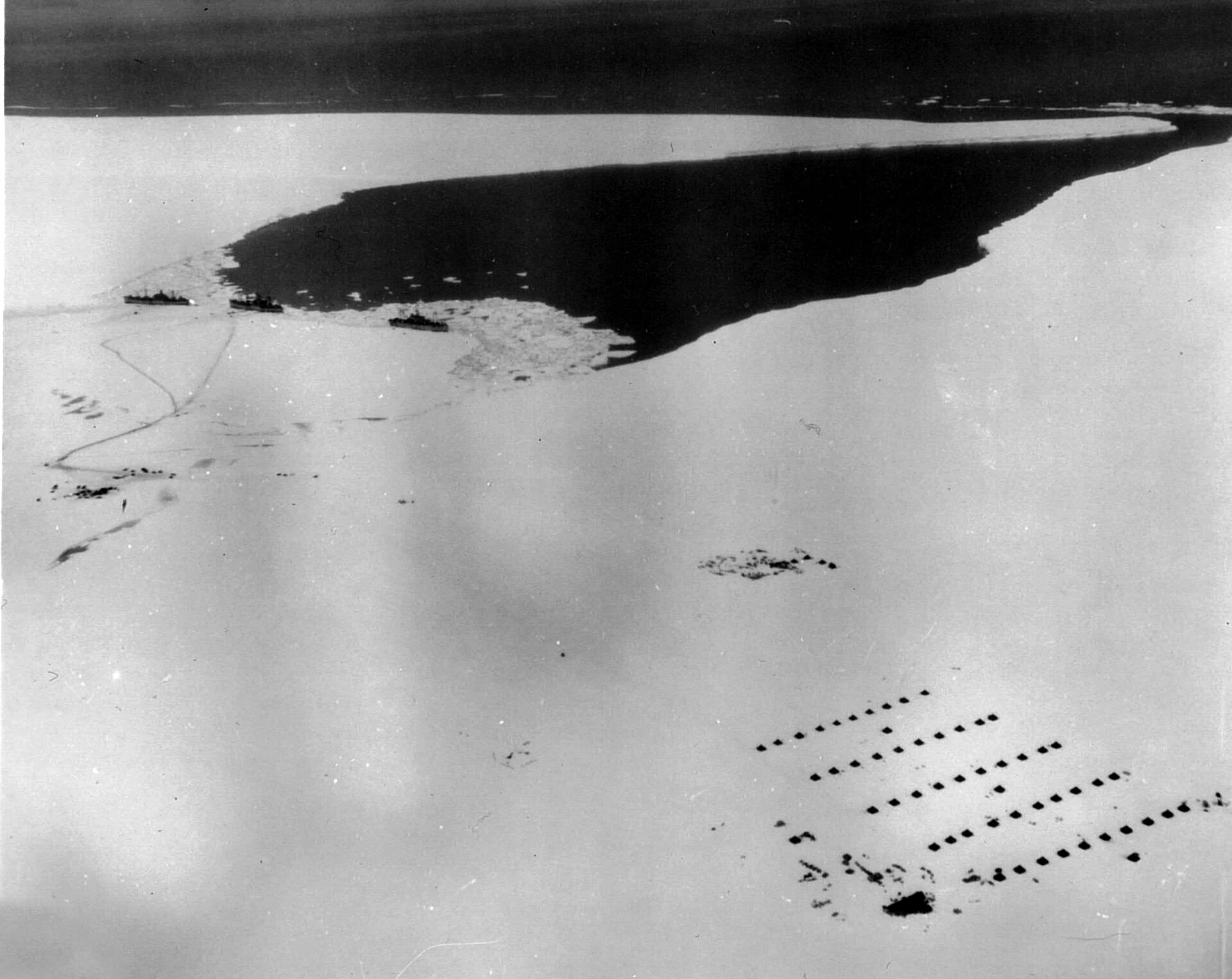 Vista aérea del campamento Little America IV en la Antártida, con tres barcos amarrados al borde del hielo